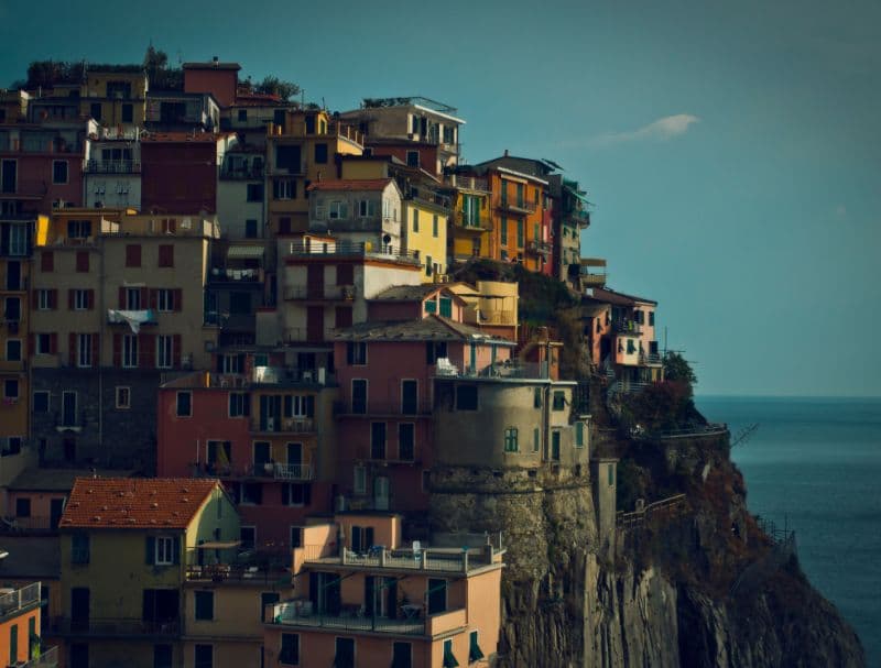 Cinque Terre A picturesque view of the colorful hillside village in Cinque Terre, Italy. Multicolored buildings are built into the steep cliff face, overlooking the deep blue Ligurian Sea under a slightly hazy sky.